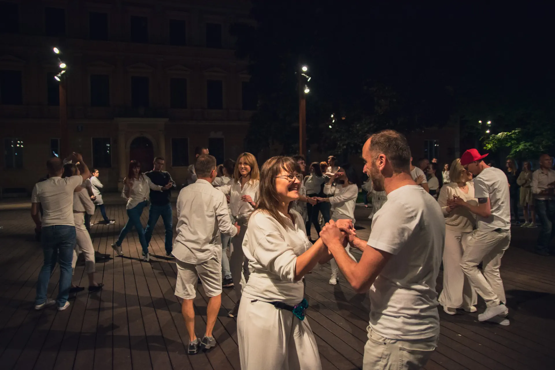Ludzie tańczą na drewnianym parkiecie.